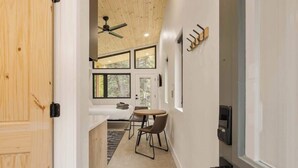A modern interior with a wooden ceiling, a small dining area with a round table and chairs, and a view of the outdoors through large windows. - Modern Mountain Studio | Hot Tub | Lostfork (Grant)