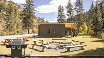 A lodge with a wooden exterior, picnic tables, a grill, and a fire pit.