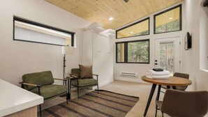 A modern room with a ceiling fan, large windows, a sofa, a table, and a lamp. - Guanella Studio Cabin | FirePit | Creek | Lostfork (Grant)