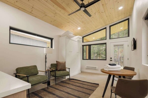 A modern room with a ceiling fan, large windows, a sofa, a table, and a lamp.