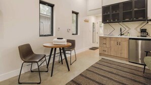 A modern kitchen with wooden cabinets, a stainless steel dishwasher, and a built-in oven. There is a round table with two chairs and a window above it. - Guanella Studio Cabin | FirePit | Creek | Lostfork (Grant)