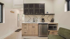 A compact kitchen with a built-in microwave, stainless steel refrigerator, and a wooden cabinet. - Guanella Studio Cabin | FirePit | Creek | Lostfork (Grant)