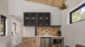 A modern kitchen with wooden cabinets, a built-in microwave, and a coffee maker. - Exclusive Basecamp Buyout | 14 Cabins | Lostfork (Grant)