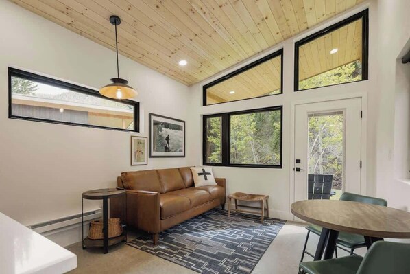 A modern living room with a leather sofa, a round wooden table, and large windows.
