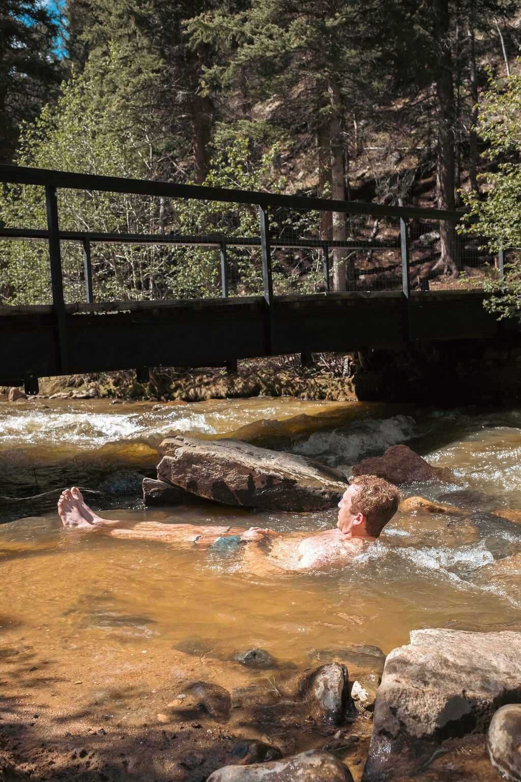 A natural setting with a bridge over a stream, surrounded by trees.