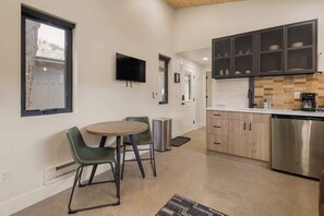 Une cuisine compacte avec un coin repas, un téléviseur fixé au mur et une grande fenêtre.