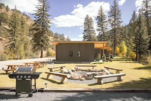 A lodge with a wooden exterior, picnic tables, a grill, and a fire pit. - Alpine Retreat | Private Hot Tub | Sauna | Lostfork (Grant)