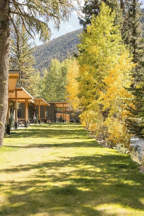 A lodge with a covered patio area, a grassy lawn, and a forested backdrop. - Alpine Retreat | Private Hot Tub | Sauna | Lostfork (Grant)