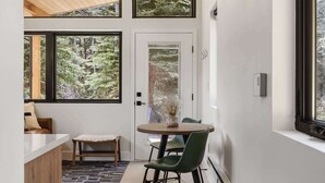A modern interior with a wooden ceiling, large windows, a dining area with a table and chairs, and a bench. - Guanella Cabin Escape | Hot Tub | Sauna | Lostfork (Grant)