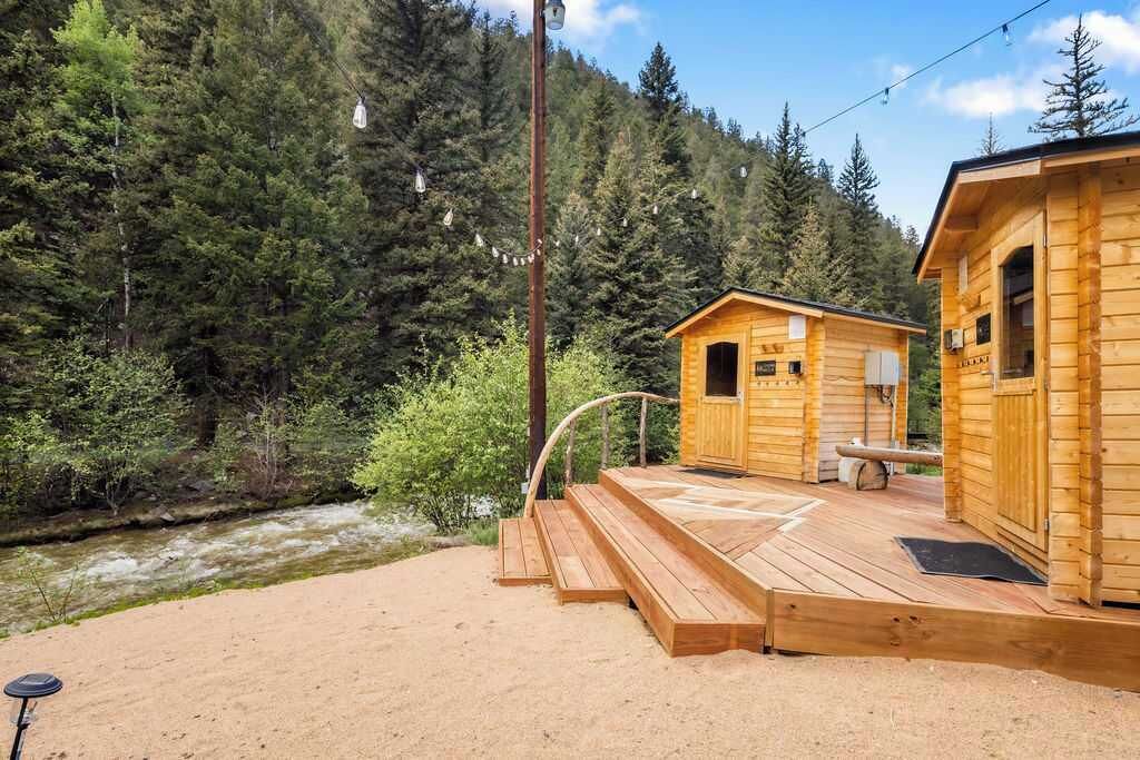 En træhytte med terrasse med udsigt over en flod, omgivet af tæt skov.