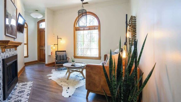 Un salón amplio con pisos de madera, chimenea, un gran ventanal de arco y una zona de estar acogedora.