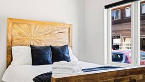 A bed with a wooden headboard, white bedding, and a view of parked cars through a window. - Golden Sanctuary | Luxe Apt | 1 Block From Main St (Golden)