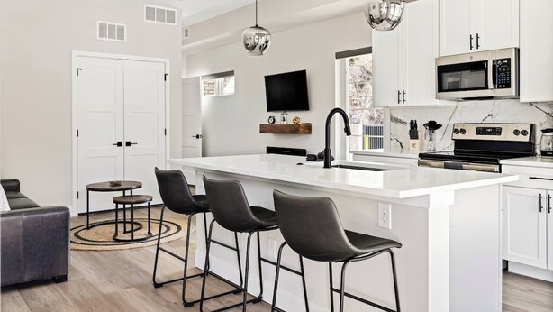 A modern kitchen with a central island, bar stools, a flat-screen TV, and a microwave. - Golden Sanctuary | Luxe Apt | 1 Block From Main St (Golden)