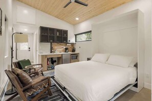 Une petite pièce comprenant un lit, un bureau, une chaise et un coin cuisine.