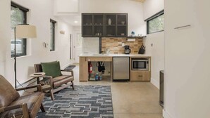 A compact kitchen with modern appliances, a built-in oven, and a microwave. There is a seating area with a sofa and a lamp.