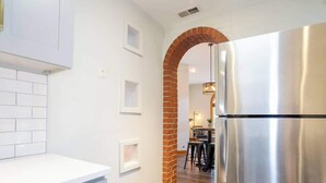 A kitchen with a stainless steel refrigerator, white cabinets, a brick archway, and a dining area in the background. - Curtis Park Club Hotel | Ultimate Group Retreat (Denver)