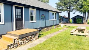 A blue building with a front porch, a stone foundation, and a picnic table in the yard.