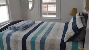 A bedroom with a bed, two windows, a round mirror, and a view of a balcony.