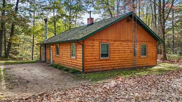 Eine Blockhütte mit grüner Dachdeckung, umgeben von Bäumen und einem Feldweg.