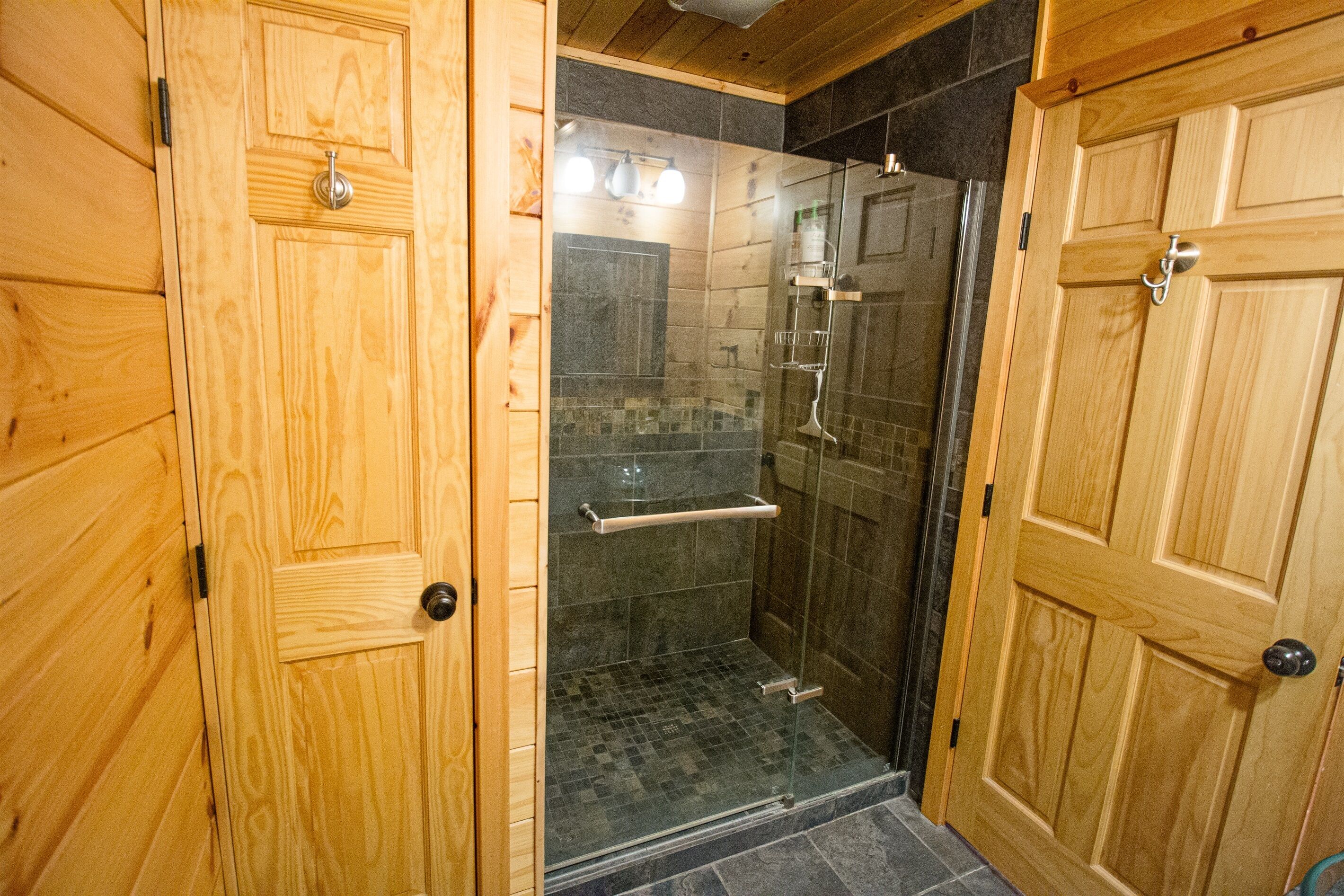 A wooden bathroom with a glass shower enclosure, a towel rack, and a door with a handle.