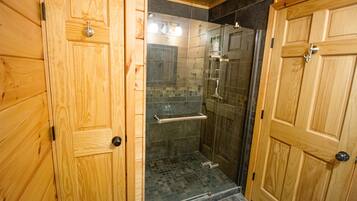 A wooden bathroom with a glass shower enclosure, a towel rack, and a door with a handle.