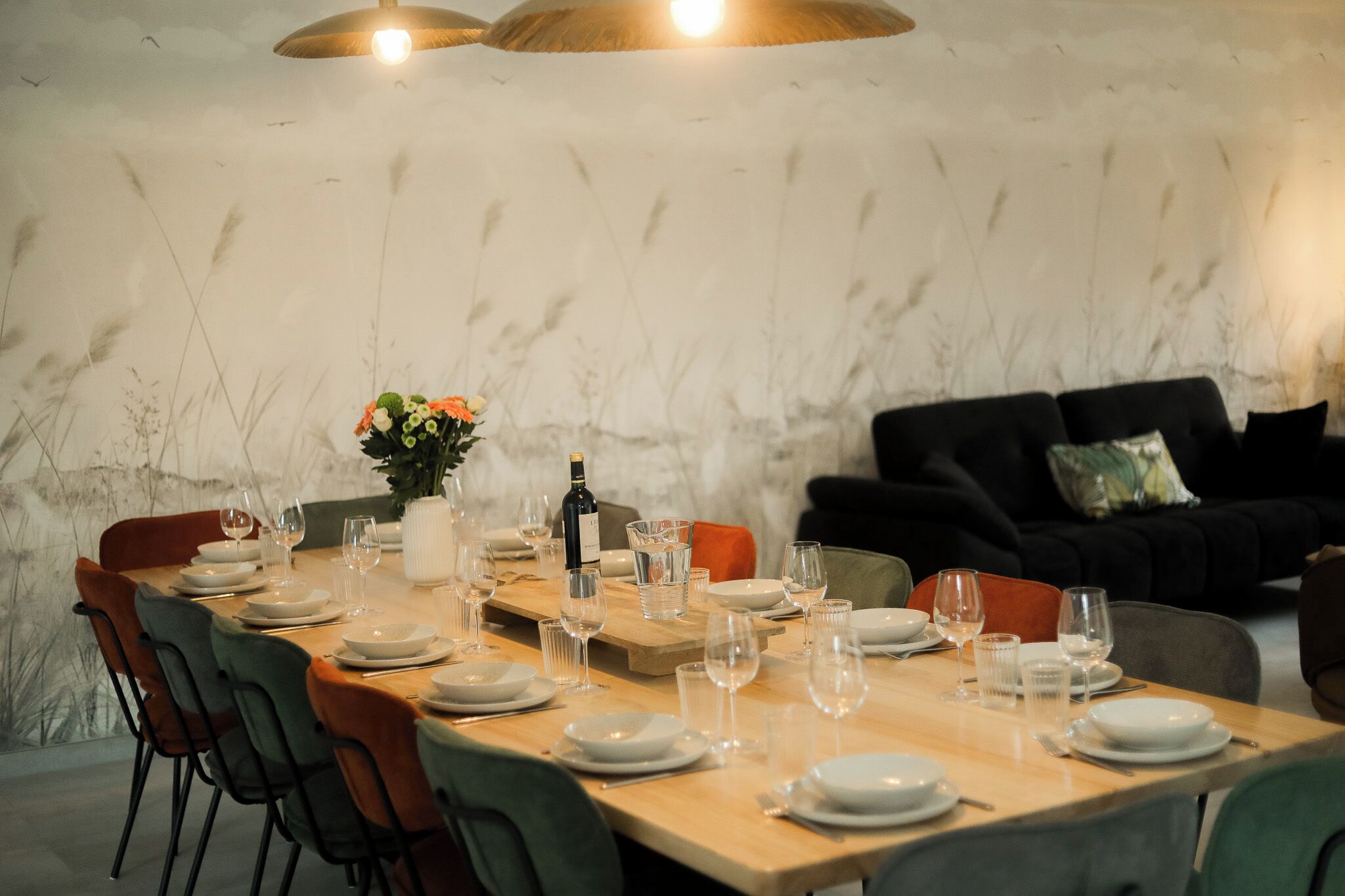 A dining table set for six with chairs, a vase of flowers, and a bottle of wine.