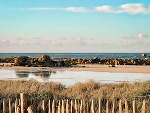 Une plage avec une clôture en bois au premier plan, une côte rocheuse et une eau calme.