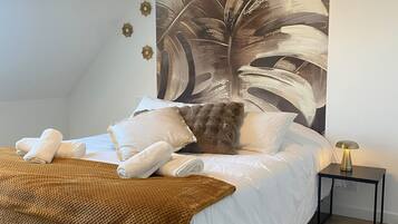 Een slaapkamer met een groot bed, een bruine plaid, witte kussens en een wanddecoratie van bladeren.
