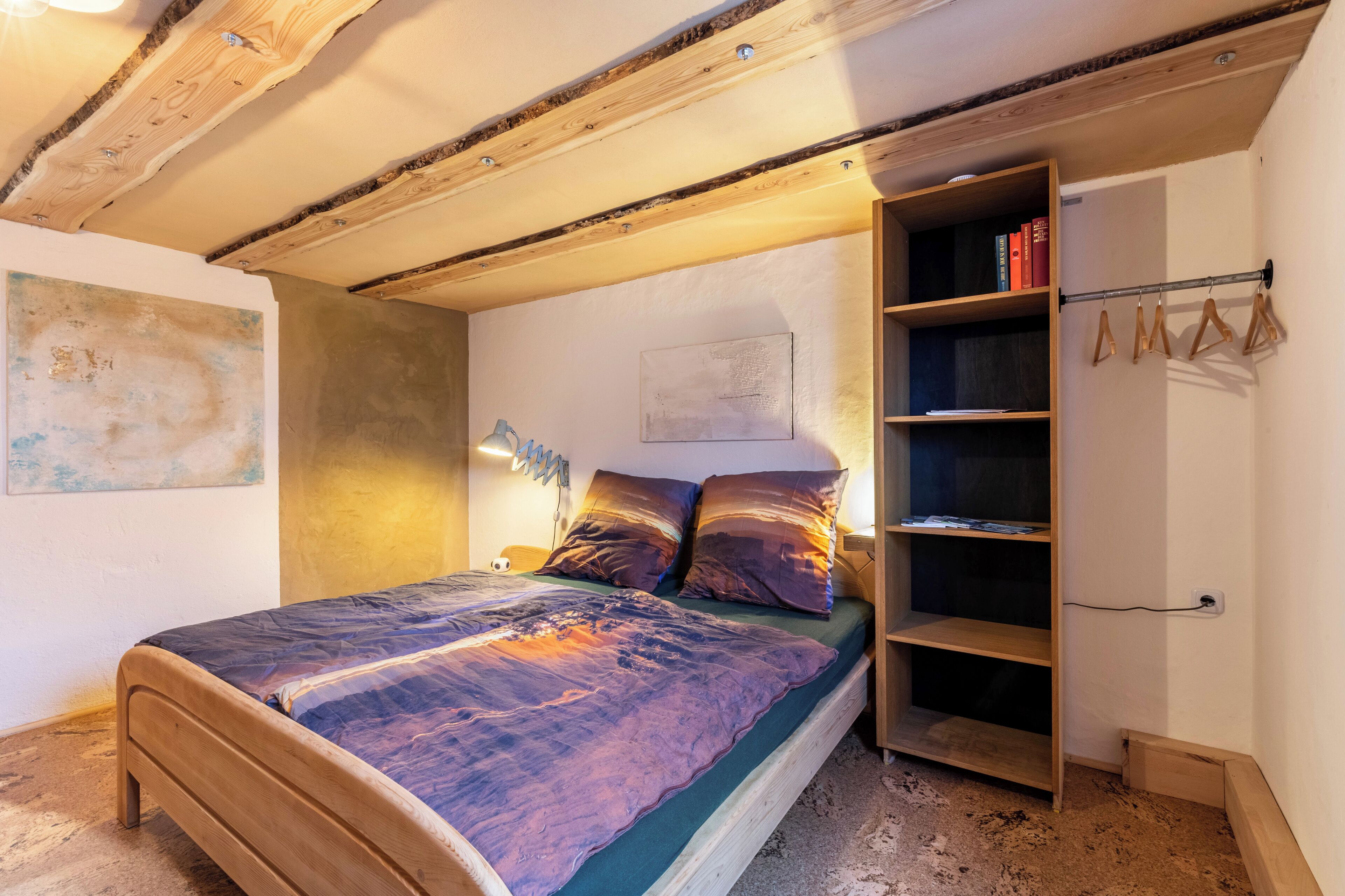 Ein Schlafzimmer mit einem hölzernen Bett, einem Nachttisch, einem Bücherregal und einer Pendelleuchte.