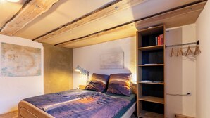 A bedroom with a wooden bed, a nightstand, a bookshelf, and a hanging light fixture.