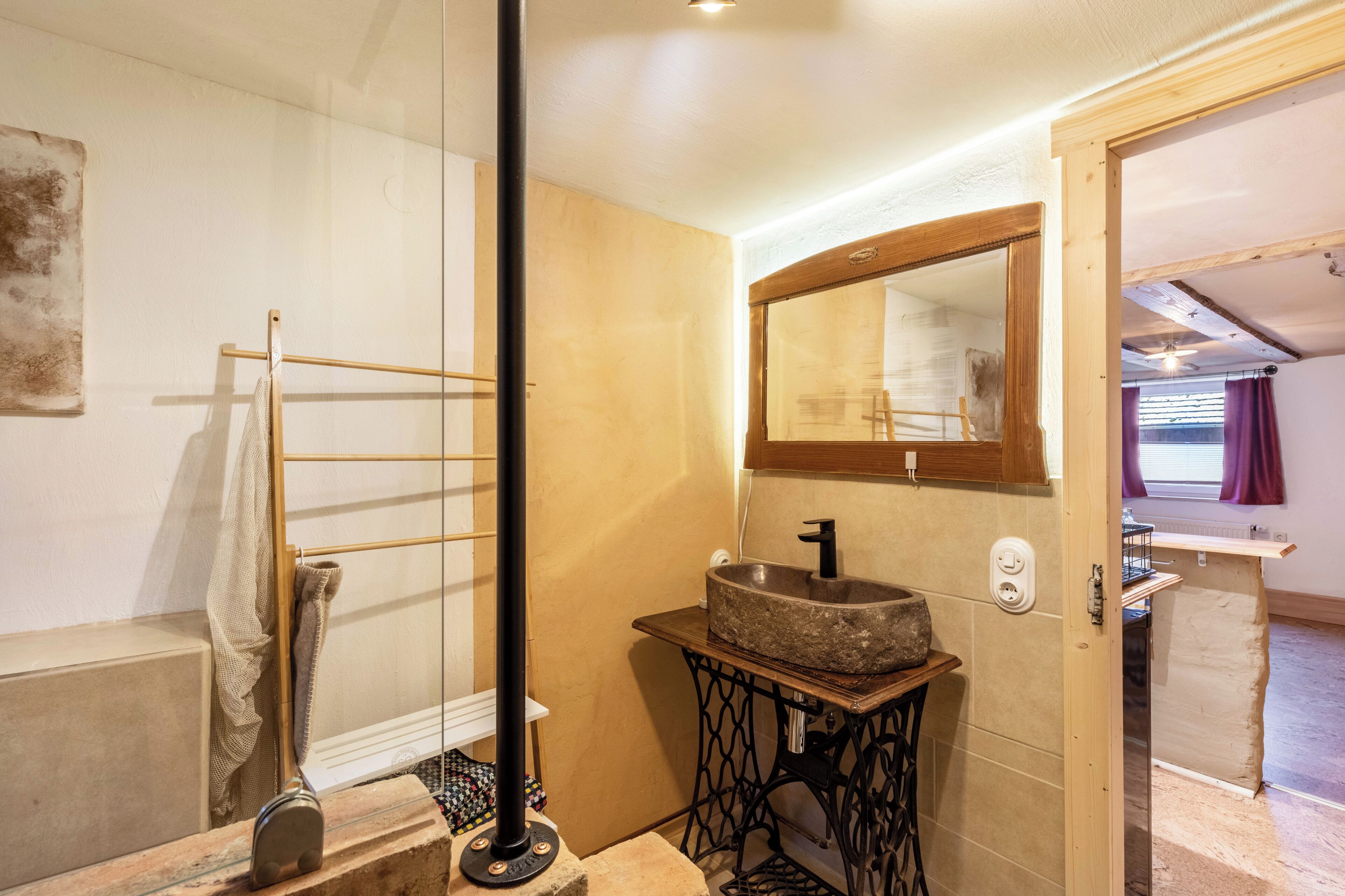 A bathroom with a stone sink, a wooden-framed mirror, and a towel rack.