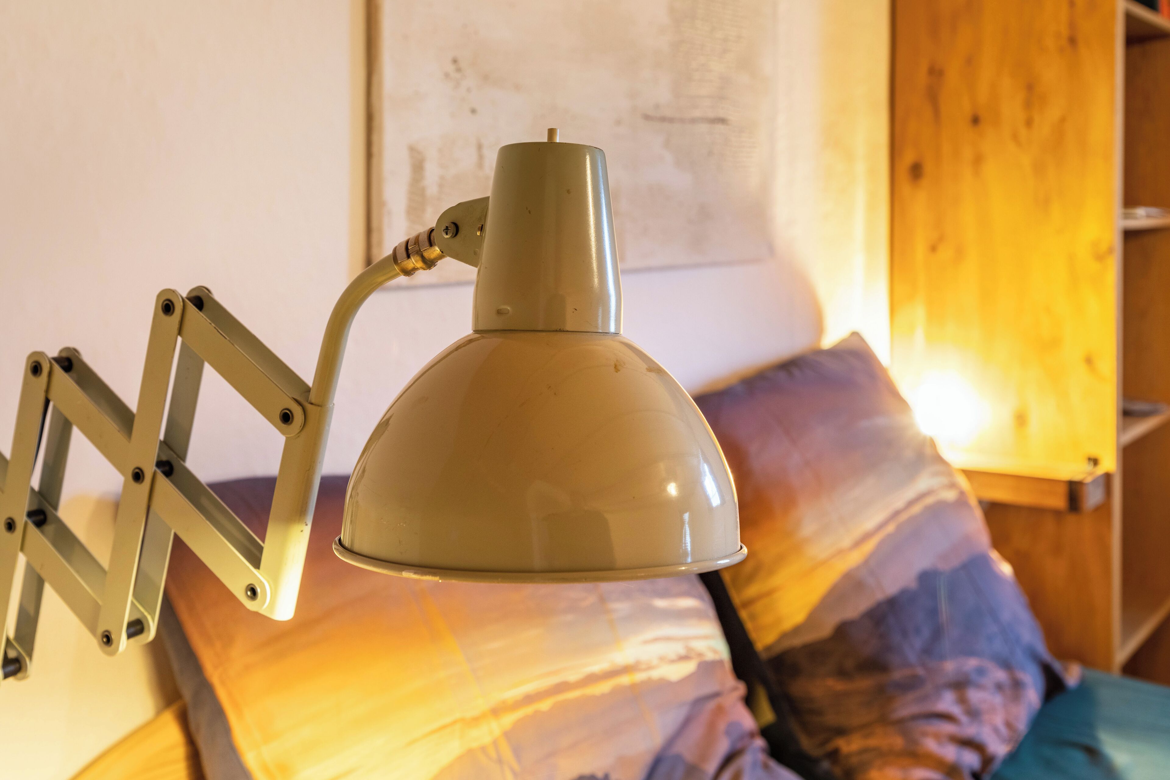 Een bed met een metalen lamp ernaast, een houten hoofdbord en een schilderij aan de muur.