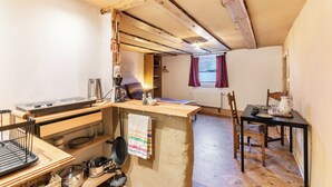 A rustic kitchen with wooden beams, a dining table, and basic kitchen appliances.