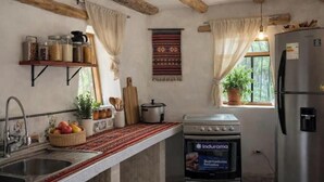 A kitchen with a stove, refrigerator, and a window with curtains.