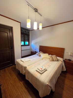 Ein Doppelbett mit Holz-Kopfteil, zwei Nachttische, ein Fenster mit Jalousien und eine Deckenleuchte.