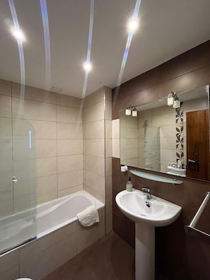 A modern bathroom with a glass-enclosed shower, a white sink, and a large mirror.