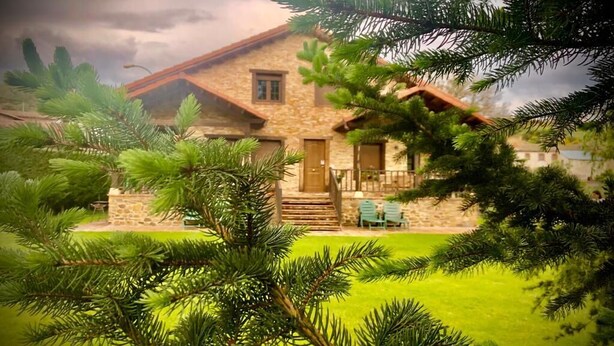 A stone house with a wooden roof, a front porch, and a small lawn. - Gîte casa lara with swimming pool lagunas (San Martín de valdetuejar)