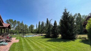A well-maintained lawn with a pool, surrounded by tall trees and a wooden deck. - Gîte casa lara with swimming pool lagunas (San Martín de valdetuejar)