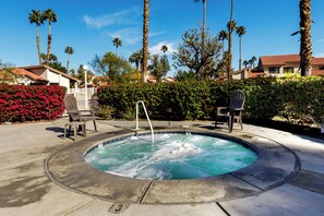 Un jacuzzi entouré de palmiers et un espace aménagé au bord de la piscine avec des chaises.