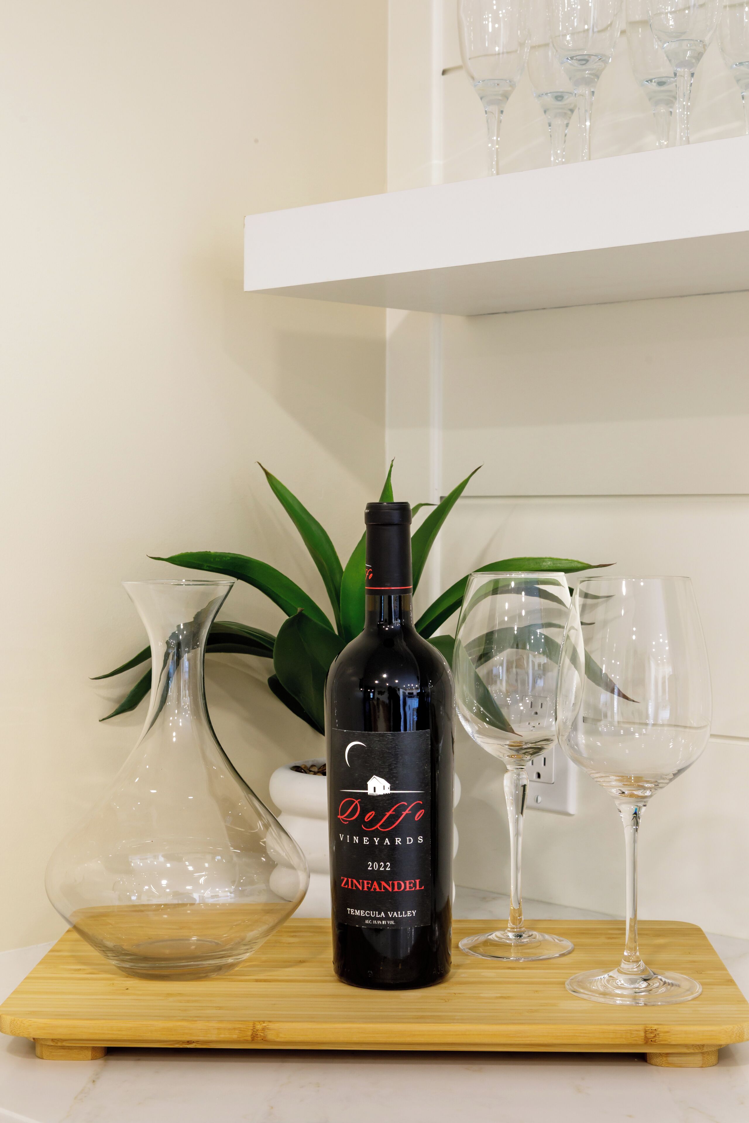 Una bottiglia di vino, due bicchieri e una brocca su un tagliere di legno.