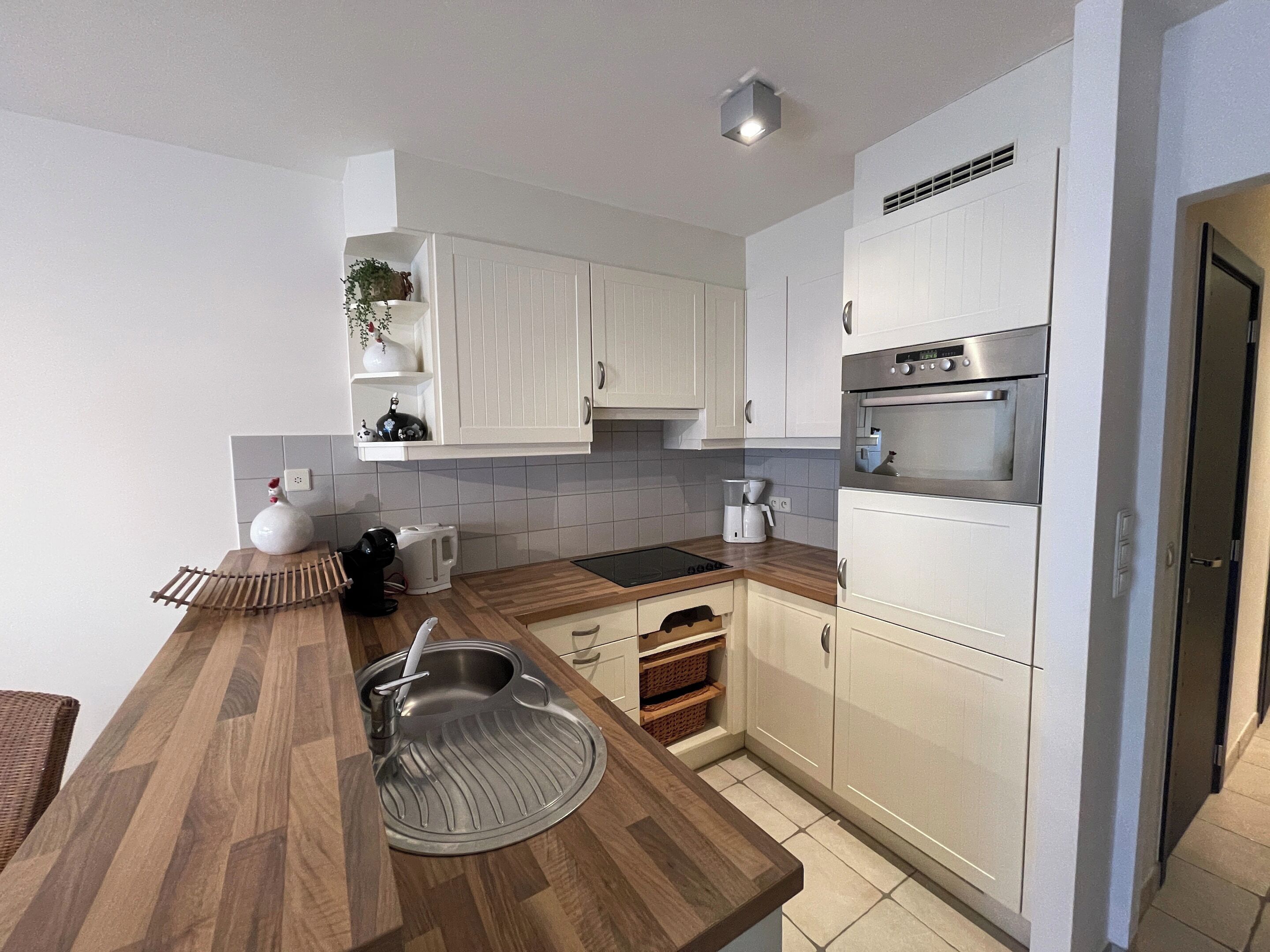 A modern kitchen with white cabinets, a wooden countertop, a built-in sink, and a stainless steel oven.