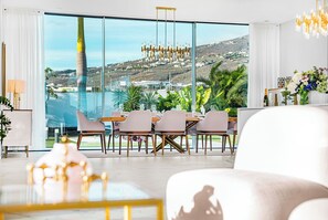 A modern dining area with a large table and chairs, large windows with a view of a city and hills, and a chandelier. - Luxury Villa with heated Pool & Jacuzzi Near Costa Adeje Golf (Adeje)