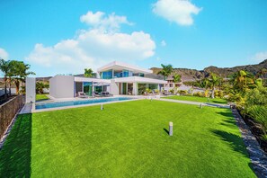 A modern house with a swimming pool, lush green lawn, and mountains in the background. - Luxury Villa with heated Pool & Jacuzzi Near Costa Adeje Golf (Adeje)