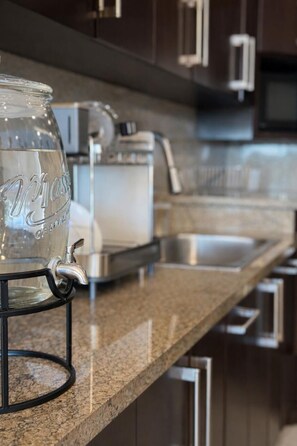 A kitchen with a stainless steel sink, a coffee maker, and a glass jar with a pump.