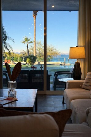 Ein Zimmer mit Blick auf einen Pool und Palmen, ein Tisch mit einer Lampe sowie ein Sofa.