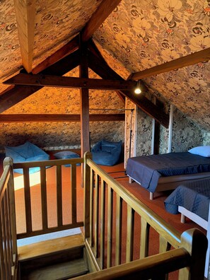 Quarto no sótão com escada de madeira, duas camas e uma poltrona de couro azul.