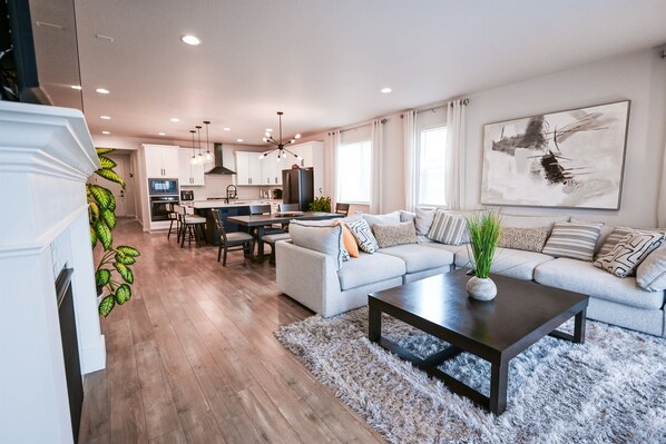 A modern living room with a sofa, coffee table, and a dining area with chairs and a table. - Lux Family Retreat|Pool Table|13 Min to Airport (Commerce City)