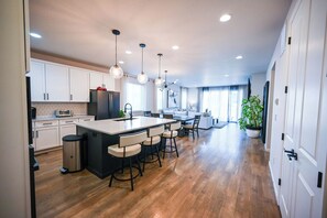 A modern kitchen with a central island, bar stools, and pendant lighting. - Big & Beautiful Home Near DIA | Fully Furnished (Commerce City)