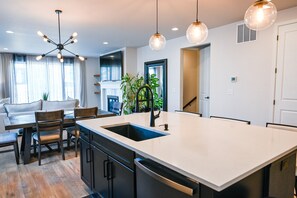 A modern kitchen with a central island, pendant lighting, and a dining area with a sofa and chairs. - Lux Family Retreat|Pool Table|13 Min to Airport (Commerce City)