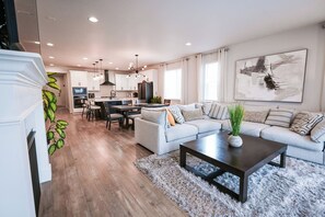 A modern living room with a sofa, coffee table, and a dining area with chairs. - Big & Beautiful Home Near DIA | Fully Furnished (Commerce City)